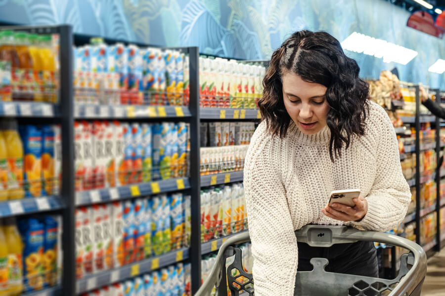Estrategias omnicanal que son - Mujer comprando en supermercado mientras revisa su celular.